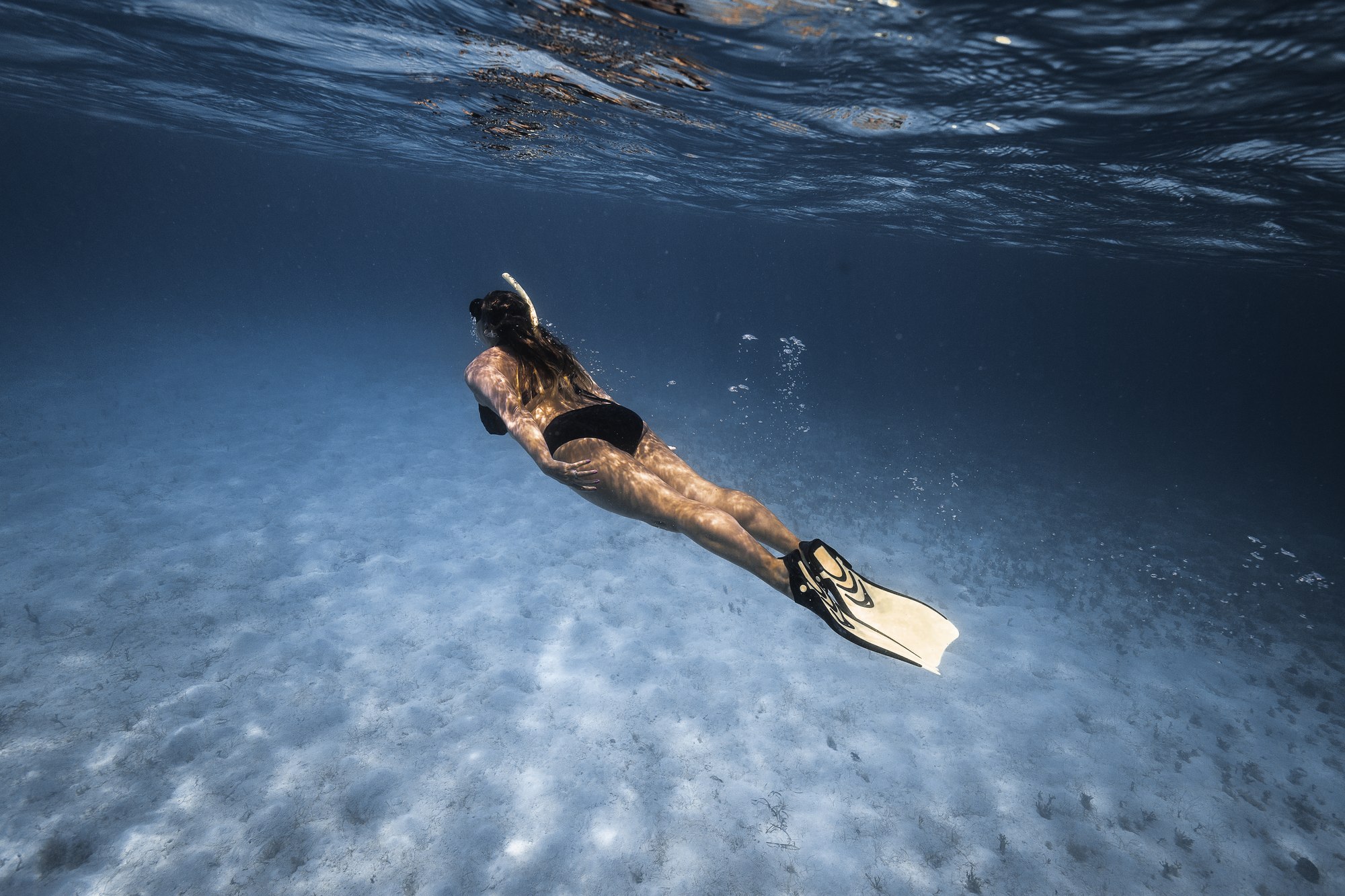 Freediver swimming underwater over a sandy seafloor